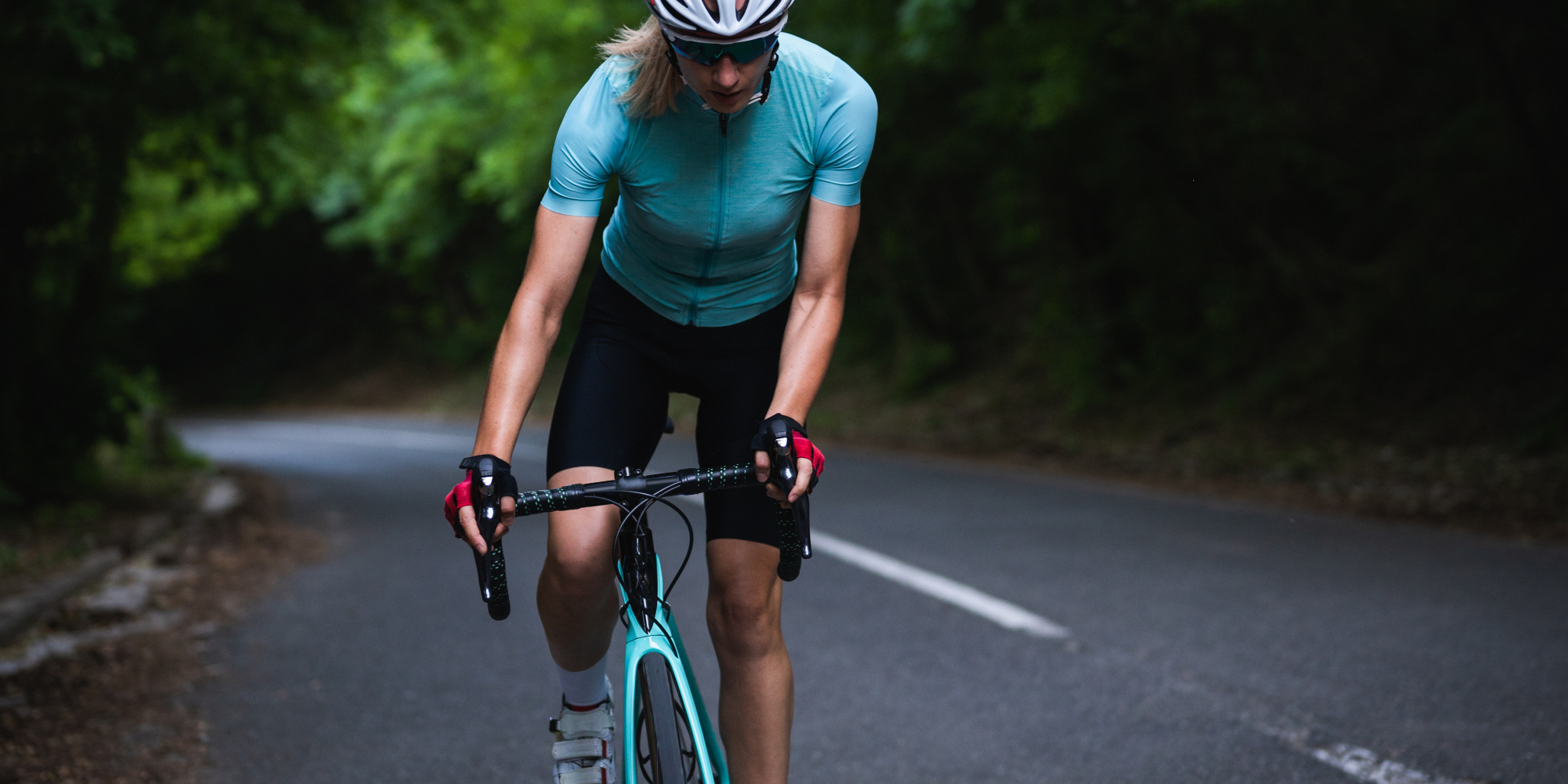 Wachse über dich hinaus mit einem Bianchi Rennrad Frau fährt auf einem Rennrad einen Berg hinauf.