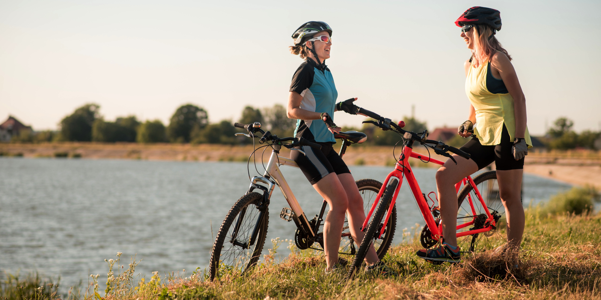 So klappt gesundes Abnehmen mit dem Rad Zwei Frauen stehen mit ihren Fahrrädern an einem Seeufer