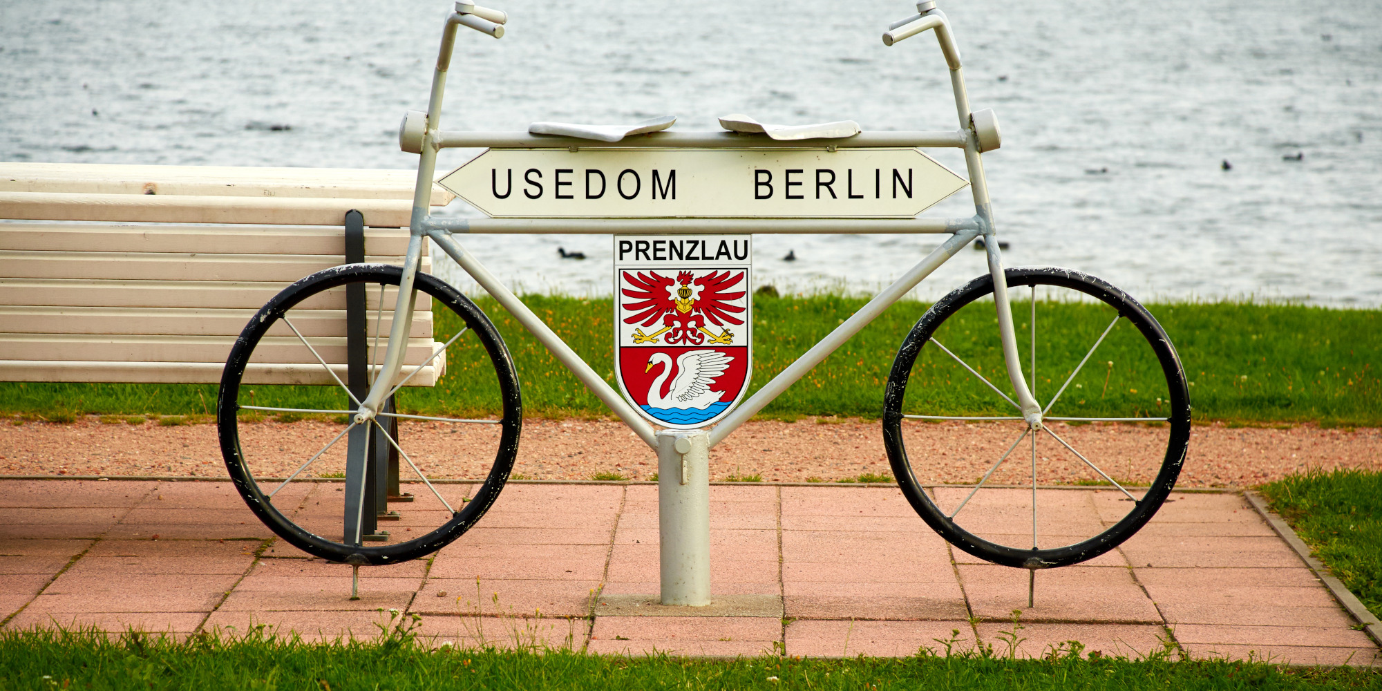 Graues Fahrrad mit einem Schild "Usedom Berlin" vor einem Wasserhintergrund.