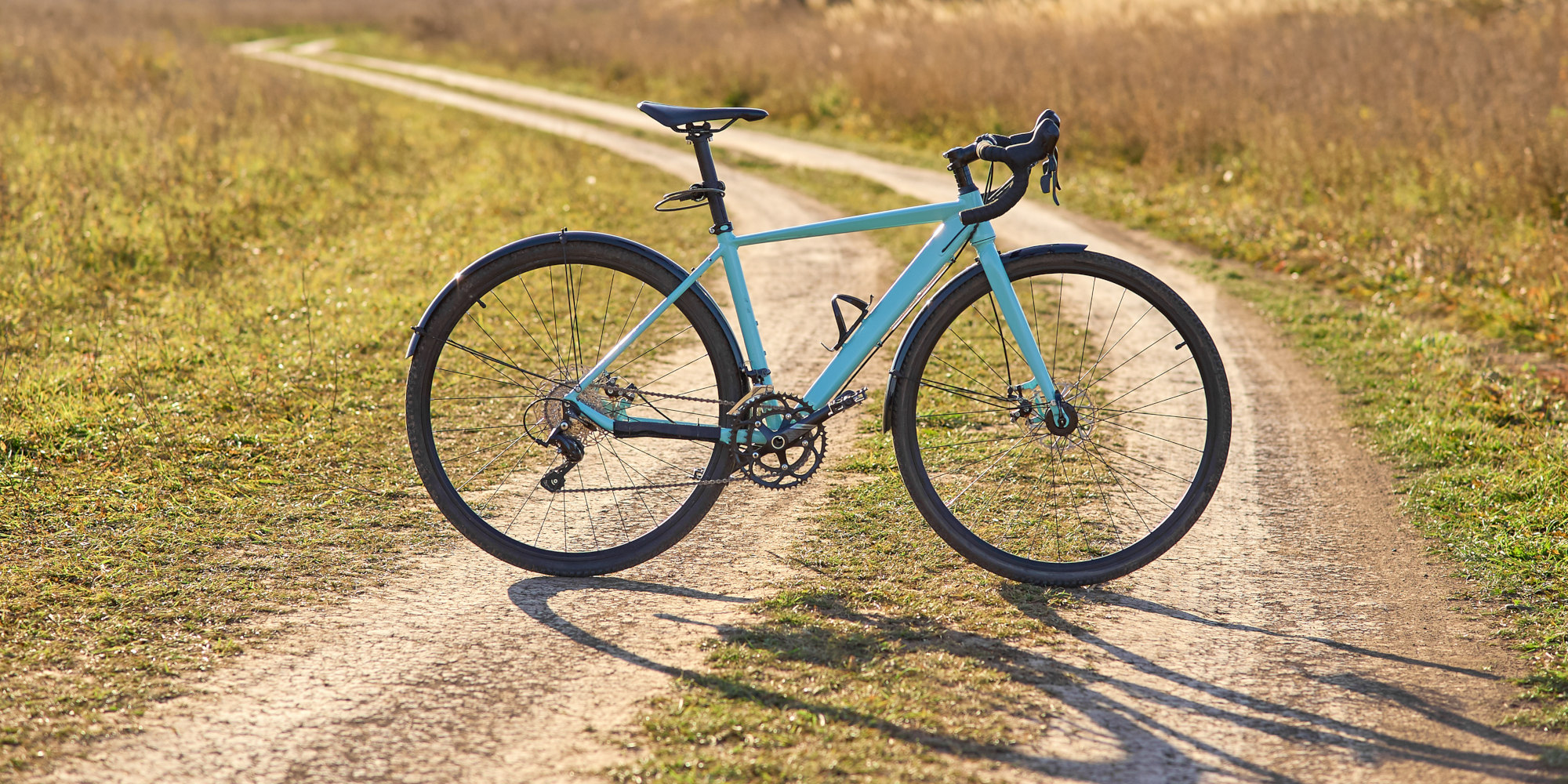 Ein hellblaues Fahrrad steht auf einem staubigen Feldweg in der Natur.