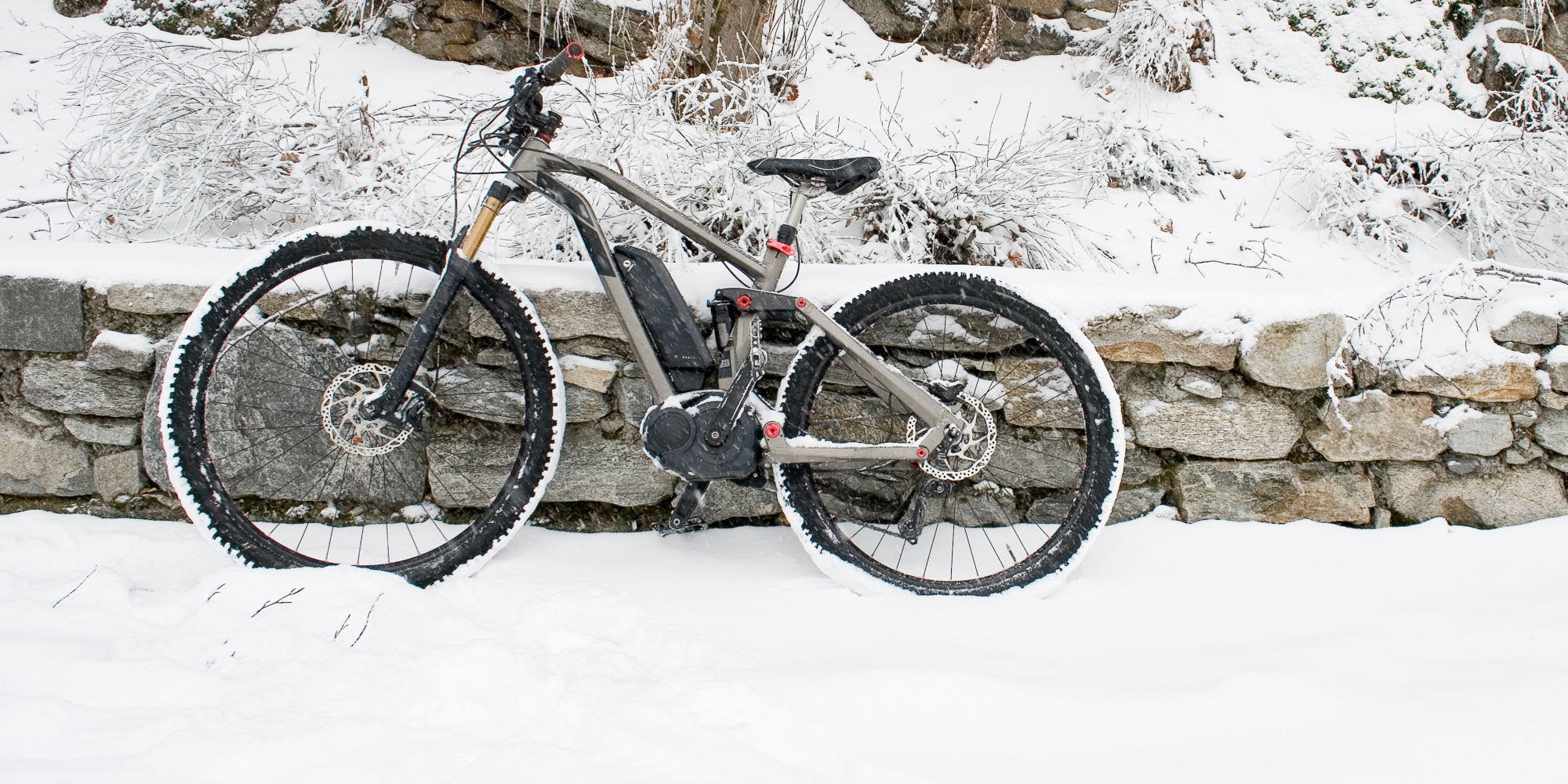 Ein Elektrofahrrad steht im Schnee neben einer Steinenmauer.