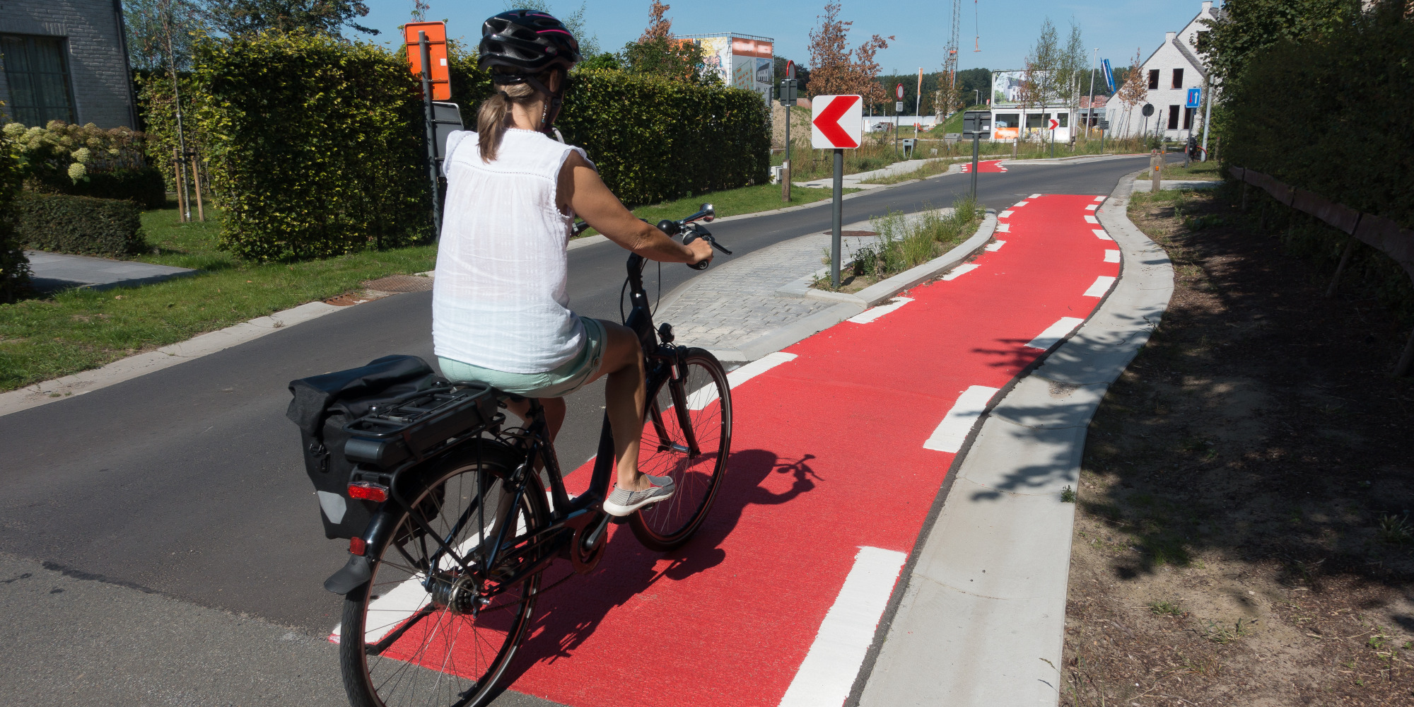 Frau auf Fahrrad auf rotem Radweg in einer Stadt, umgeben von Grünanlagen.