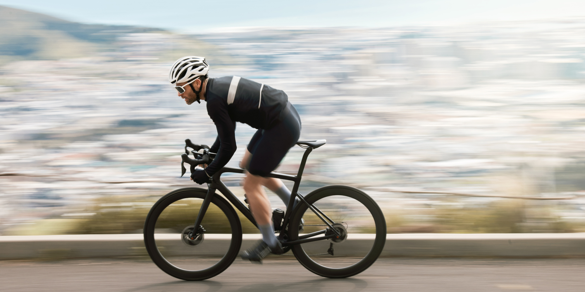 Radfahrer in sportlicher Haltung, schnell vorbeifahrend vor unscharfer Hintergrundlandschaft.