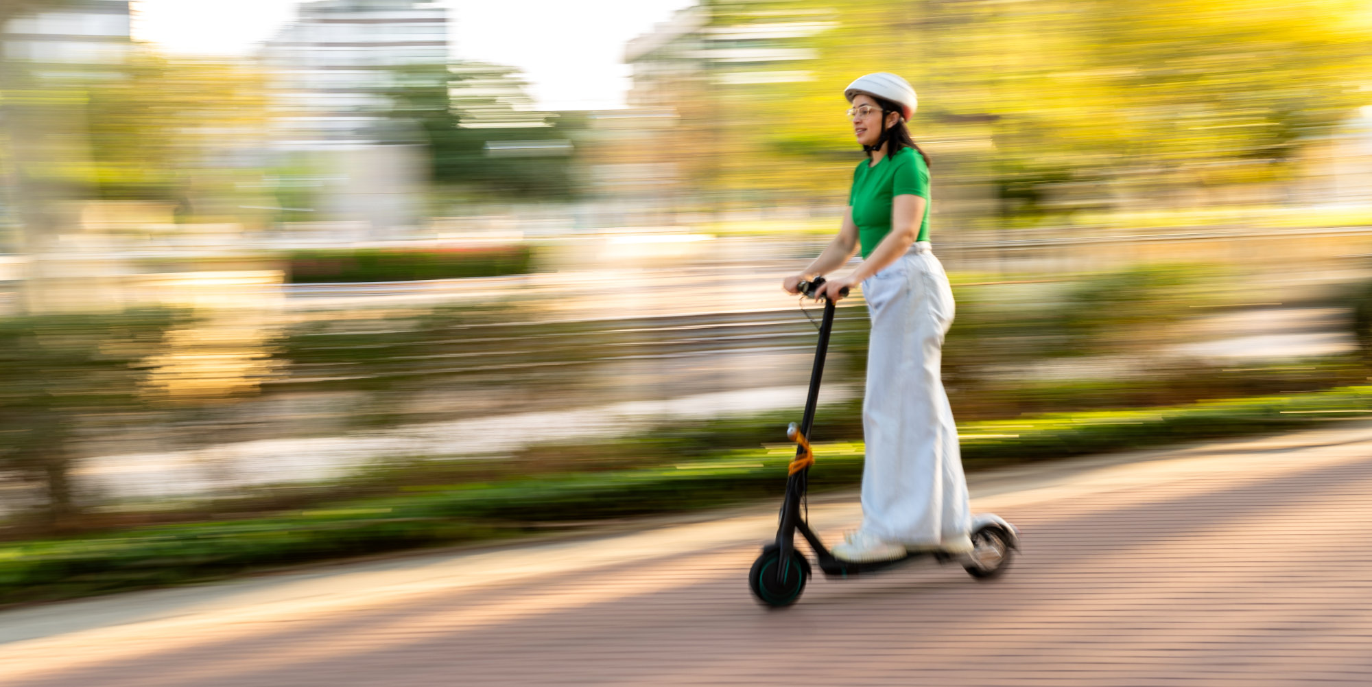 Dies sind die besten und leistungsstärksten E-Scooter Modelle. Frau mit Helm fährt mit E-Scooter über einen Weg.