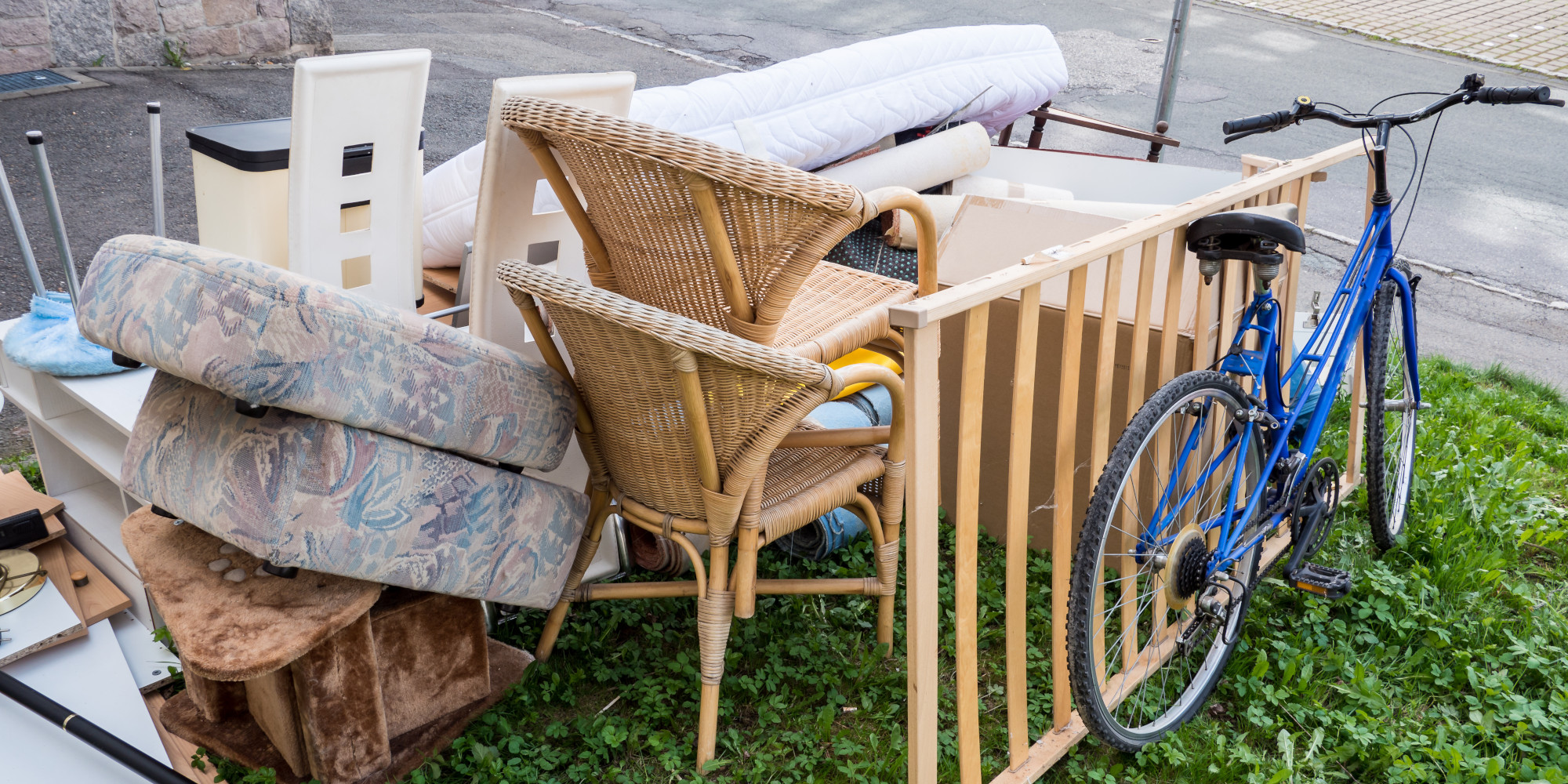 Ansammlung von Möbeln, darunter Stühle, eine Matratze und ein Fahrrad, auf grünem Gras.