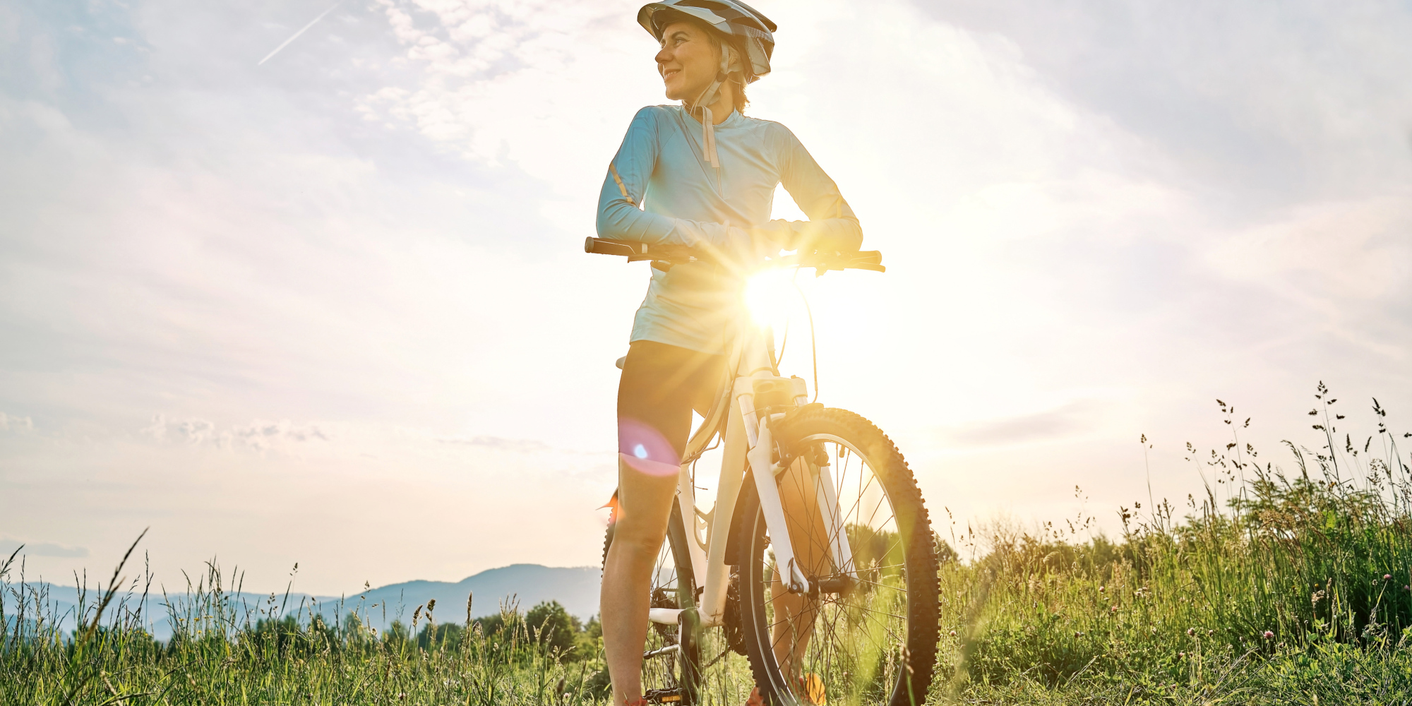 Junger Radfahrer hält an seinem Fahrrad, während die Sonne aufgeht.
