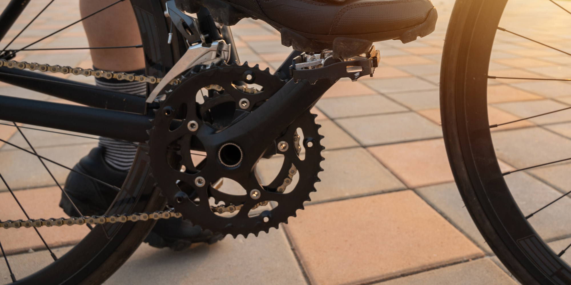 Detailaufnahme eines Fahrrad-Kurbelgelenks auf einem gepflasterten Boden.