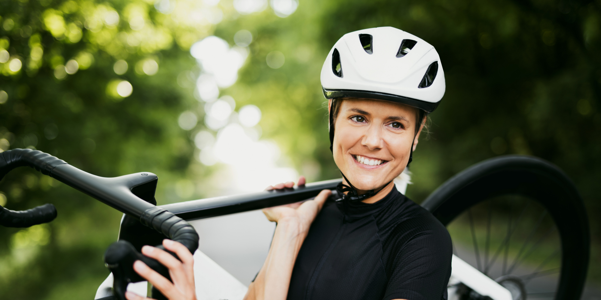 Lächelnde Fahrradfahrerin hält ihr Rad, umgeben von grüner Natur.