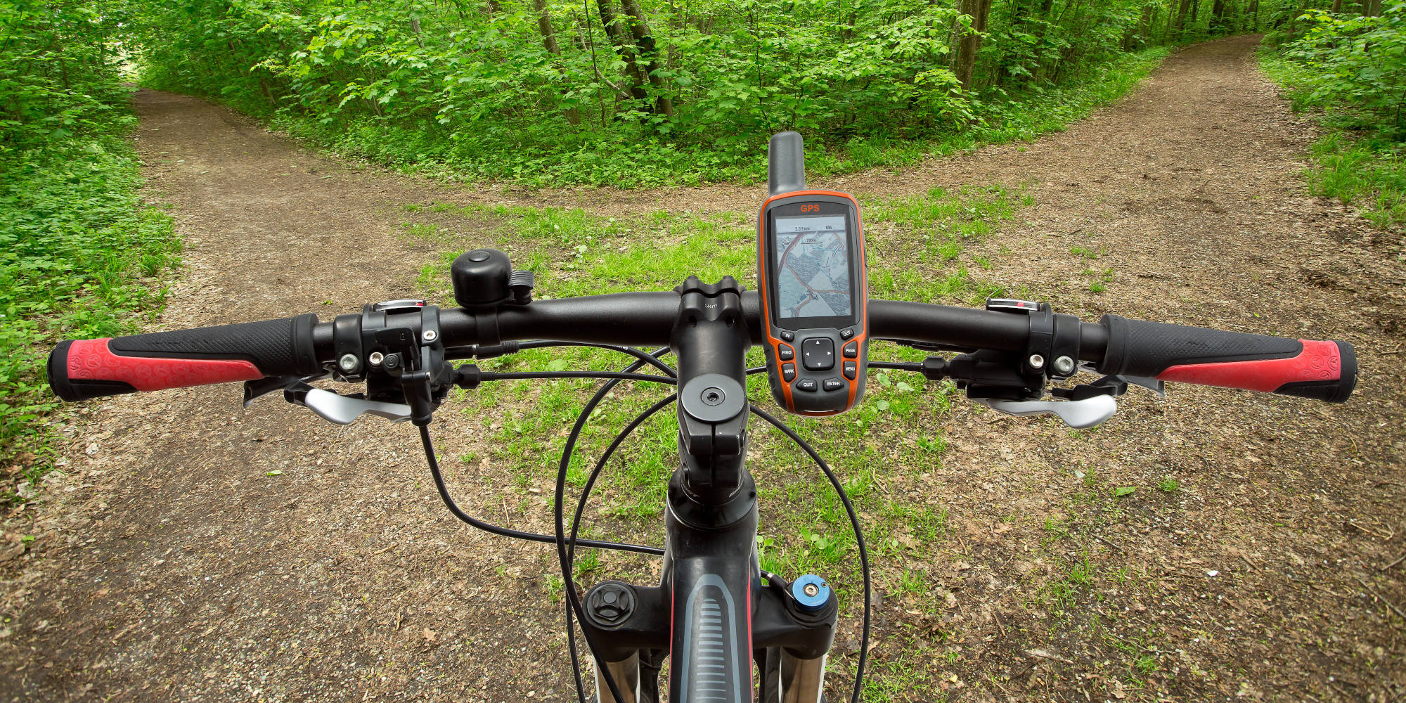 Blick von oben auf Fahrradlenker mit GPS-Gerät und Wege im Grünen.