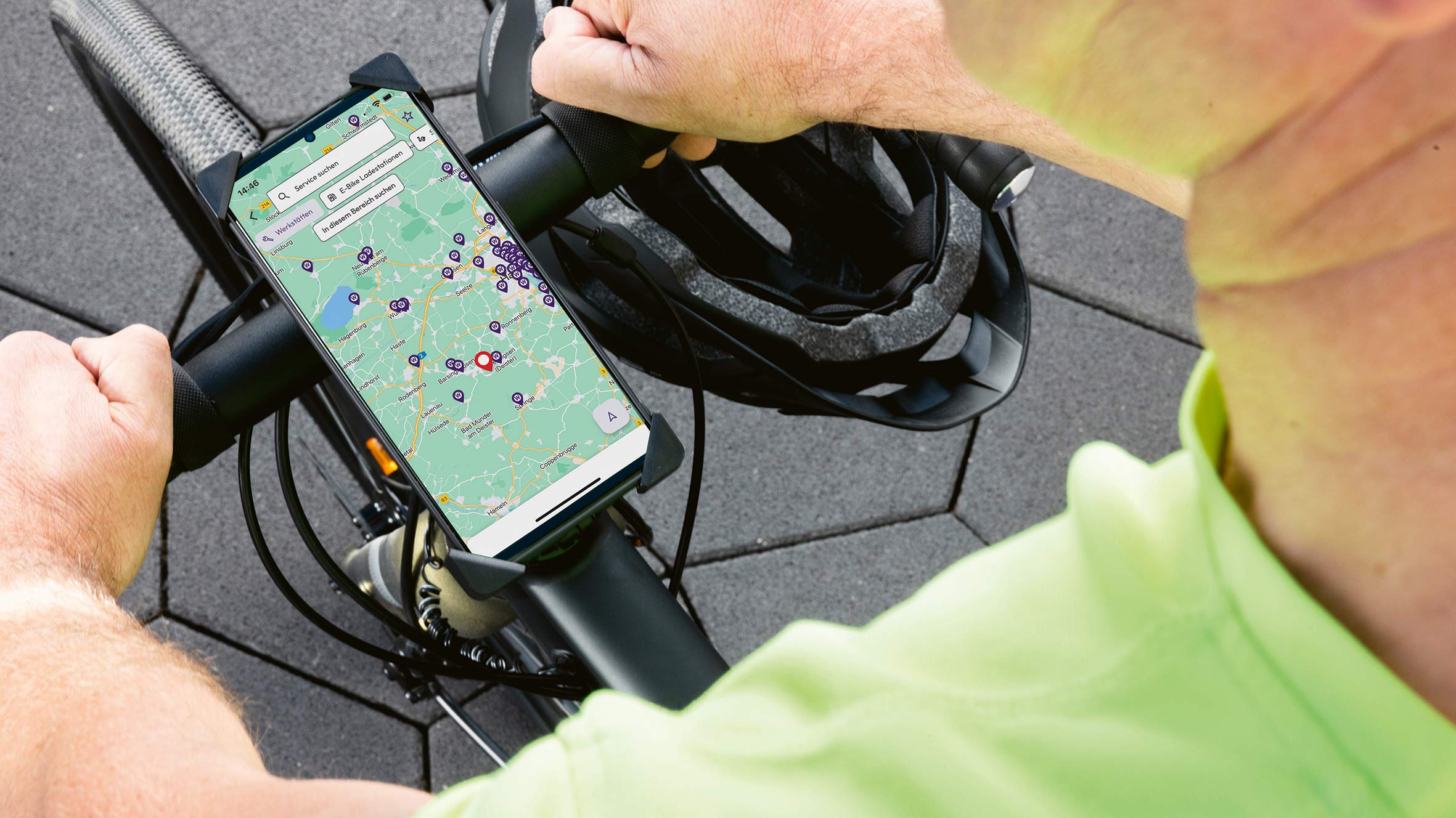 Eine Hand mit einem Smartphone auf einem Fahrradlenker, im Hintergrund ein Helm.