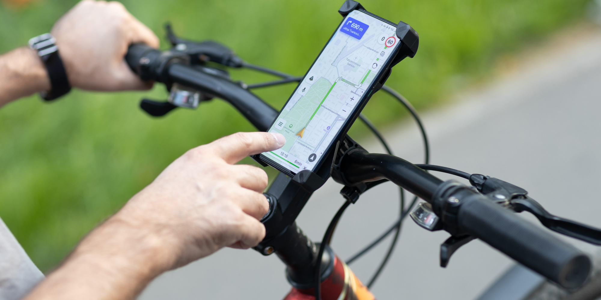 Händed, die ein Fahrradlenker halten und auf ein GPS-Gerät auf dem Handy zeigen.