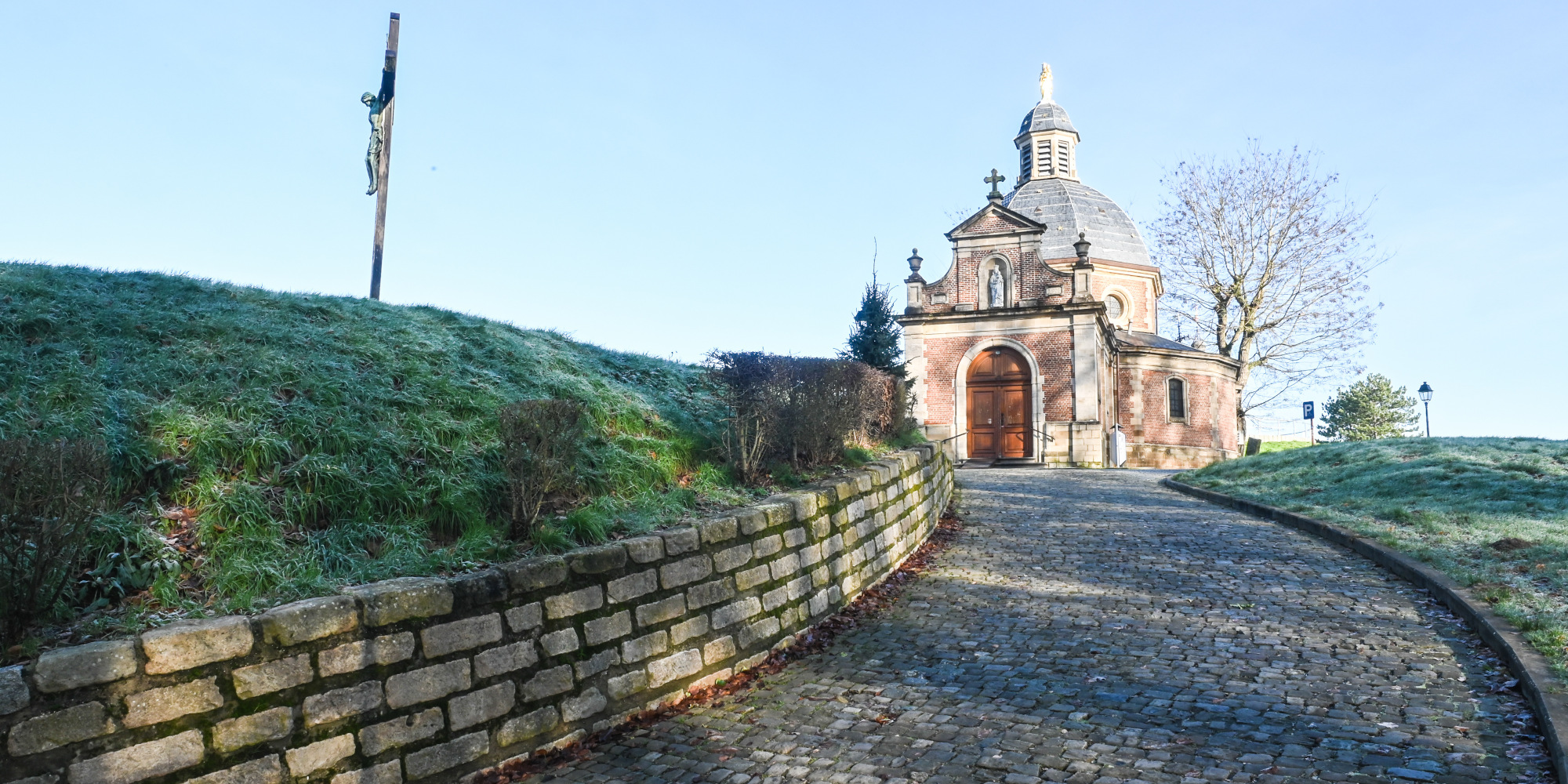 Eine neblige Wiese führt zu einer kleinen Kapelle vor blauem Himmel.