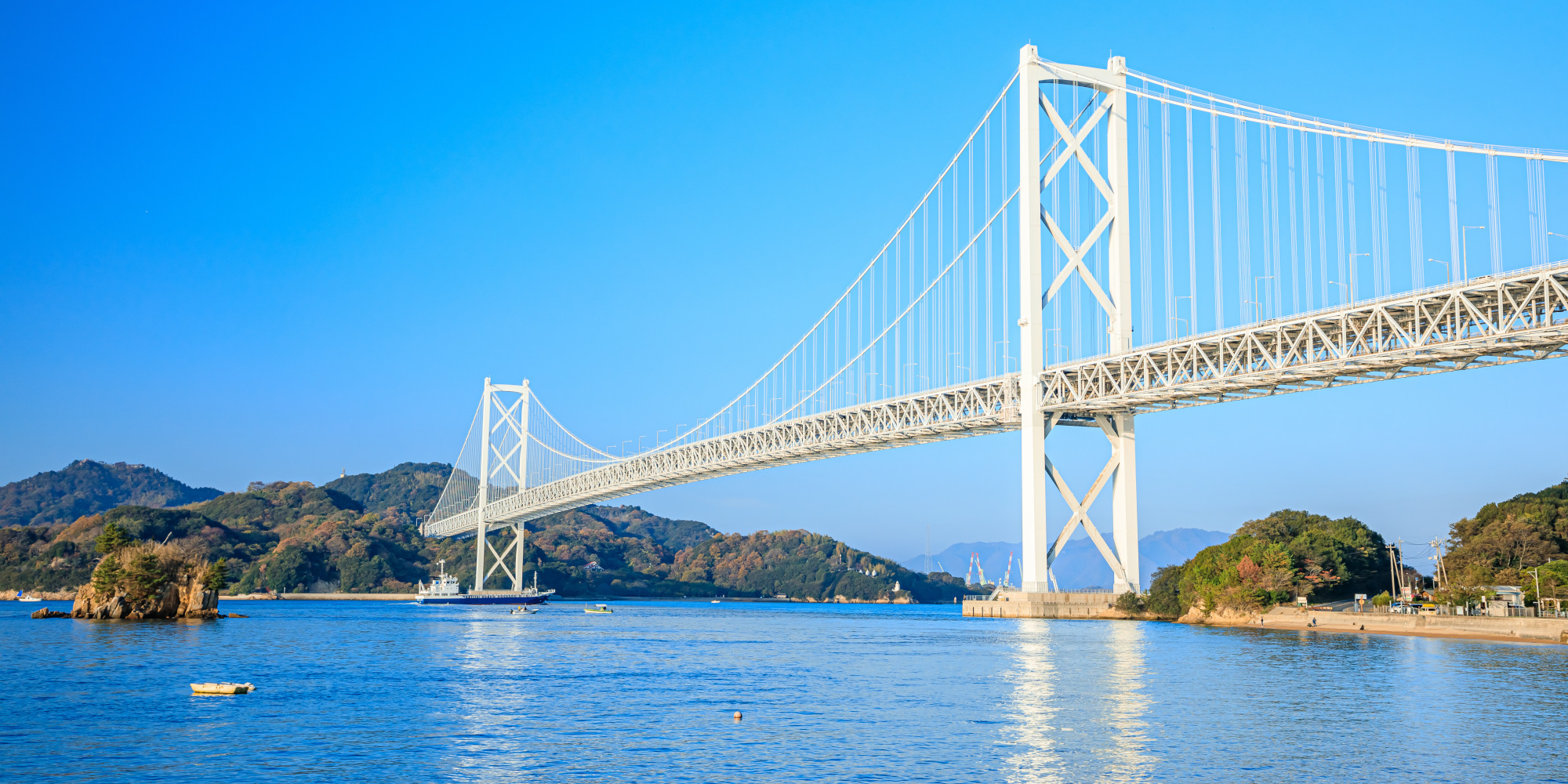 Weiße Brücke über ruhiges Wasser, umgeben von Hügeln und klarem Himmel.