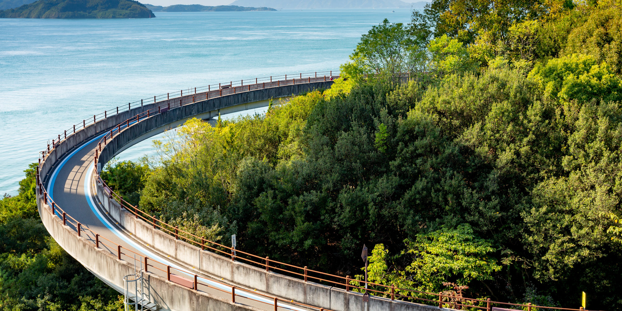 Kurvenreiche Straße umgeben von üppigem Grün mit Blick auf das Meer.