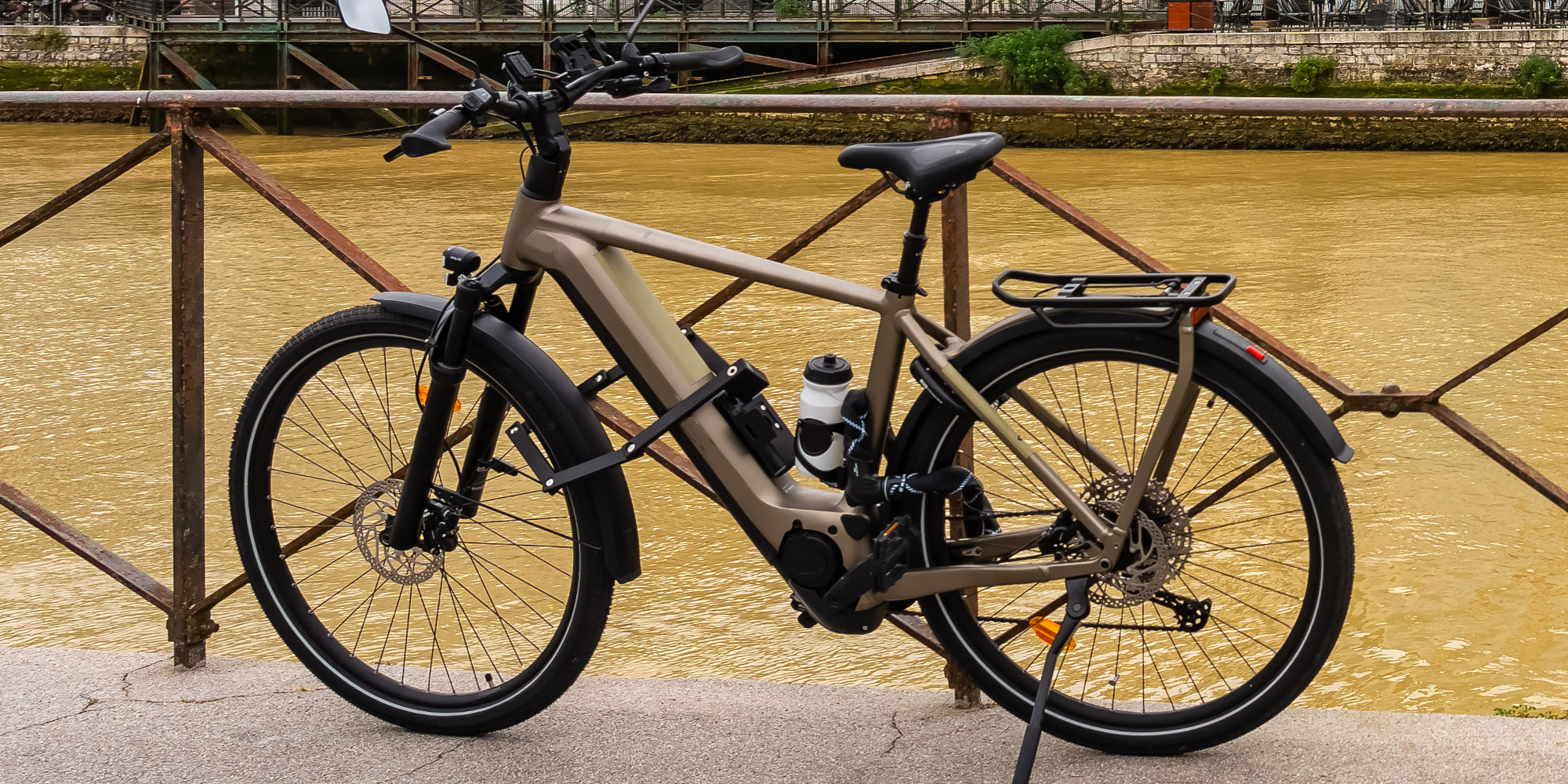 Ein modernes E-Bike steht an einem Geländer neben einem Fluss mit braunem Wasser.