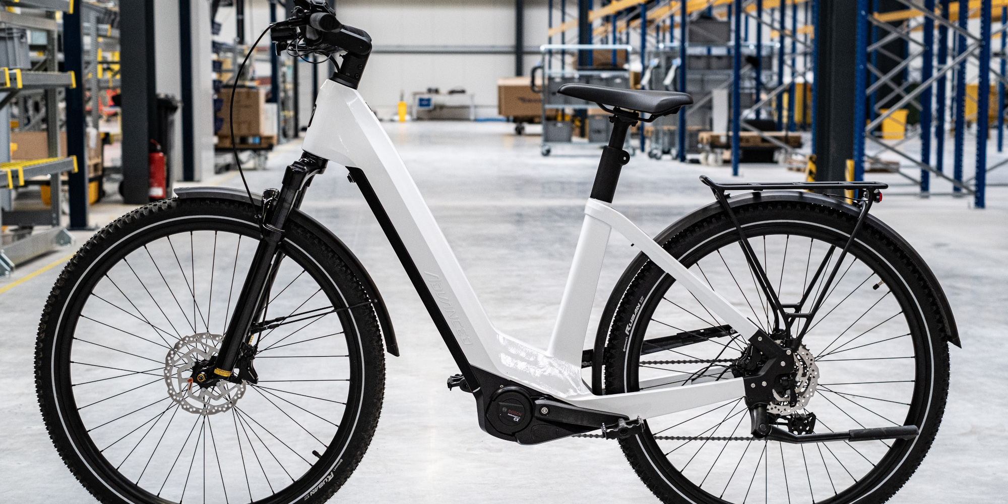 Ein modernes weißes E-Bike in einer Lagerhalle, mit Regalen im Hintergrund.