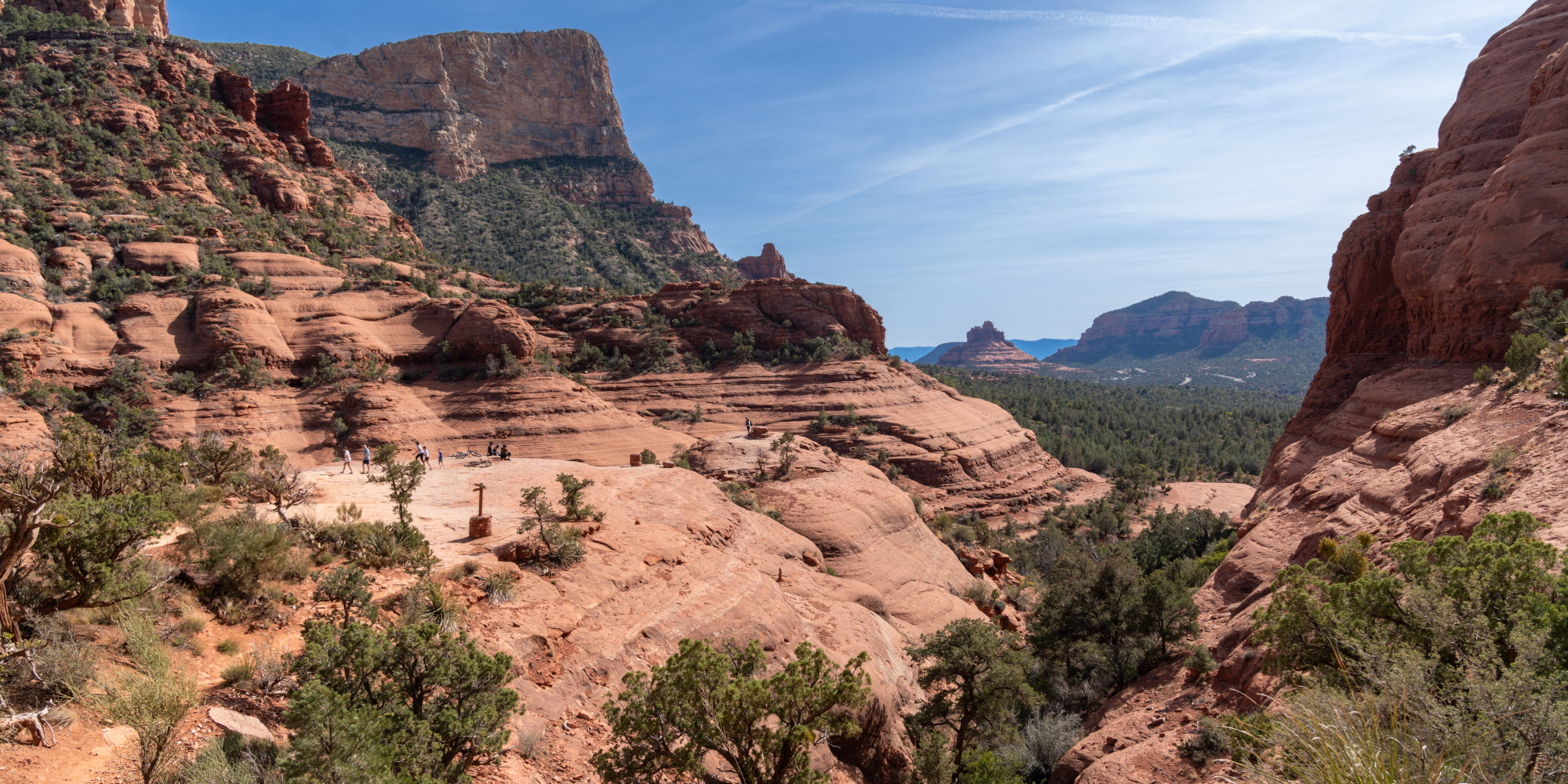 Blick auf eine hügelige, rote Felsenlandschaft mit grüner Vegetation und blauem Himmel.