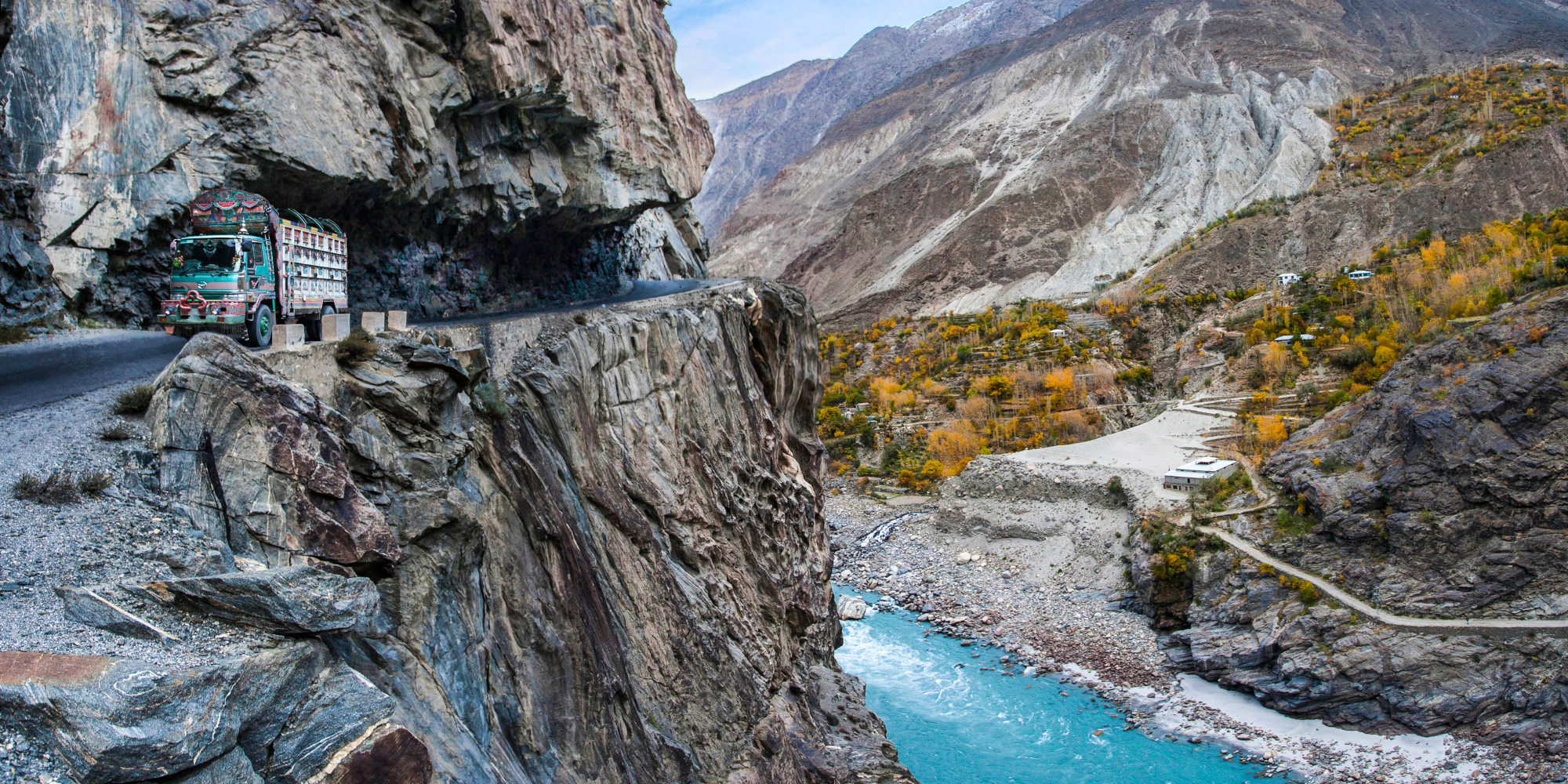 Ein Truck fährt an einer steilen Klippe entlang, mit einer türkisfarbenen Flusslandschaft im Hintergrund.