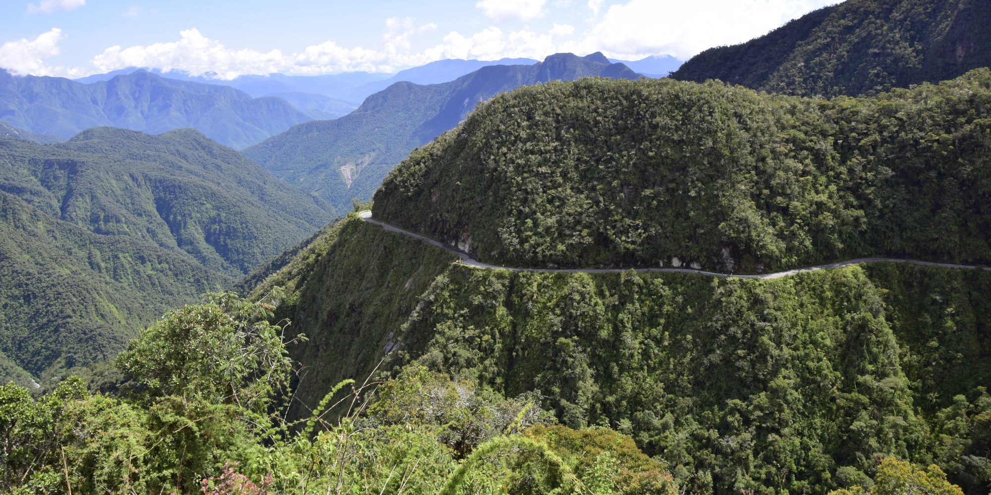 Berglandschaft mit üppigem Grün und kurvenreicher Straße im Vordergrund.