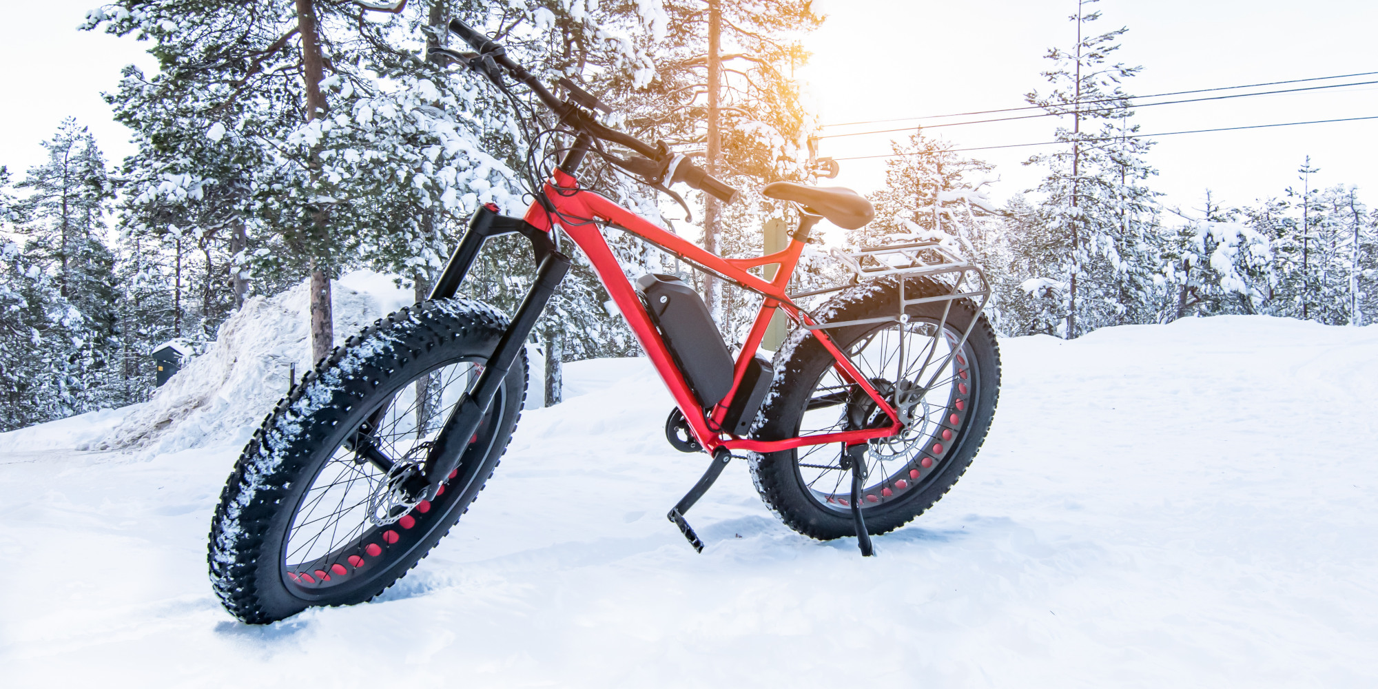 Rotes Mountainbike im Schnee vor einer winterlichen Waldlandschaft.