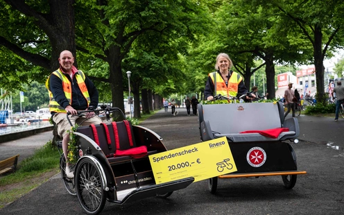 Zwei Personen in leuchtenden Westen stehen neben einem Fahrrad-Rickshaw in einem Park.