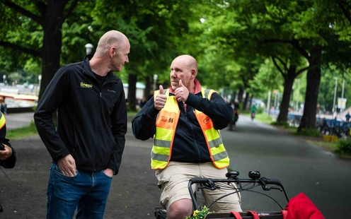 Zwei Männer unterhalten sich auf einem Weg, einer sitzt auf einem Fahrrad und zeigt Daumen hoch.