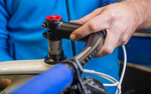 Hände montieren den Lenker an einem Fahrradrahmen in einer Werkstatt.