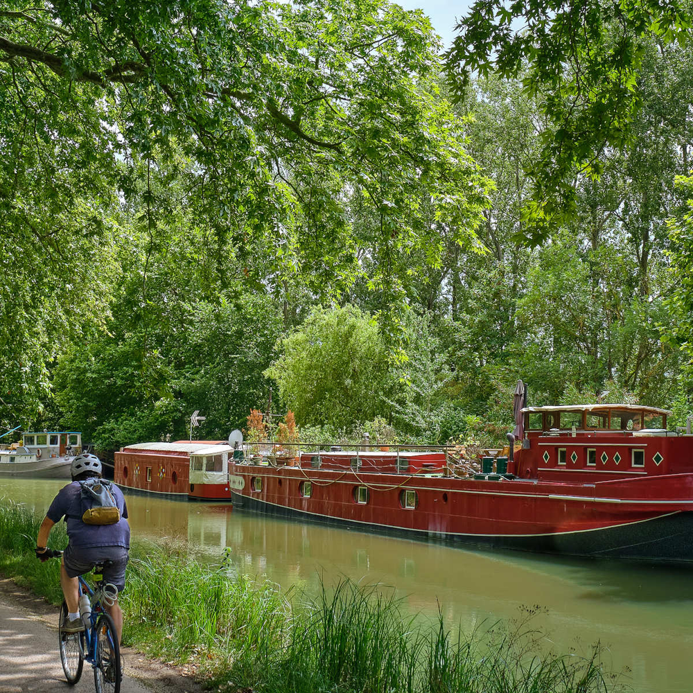 Entdecke den traumhaften Canal du Midi Radweg in Südfrankreich Radfahrer fährt am Canal du Midi in Frankreich entlang, auf dem Boote liegen.