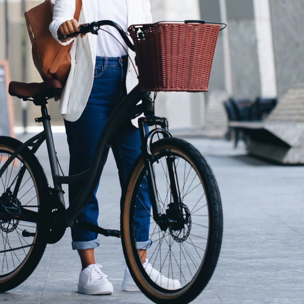 Entdecke die Vorteile eines Fahrradkorbs am Fahrrad Person steht mit einem Fahrrad in der Stadt, dass einen Fahrradkorb vorne hat.