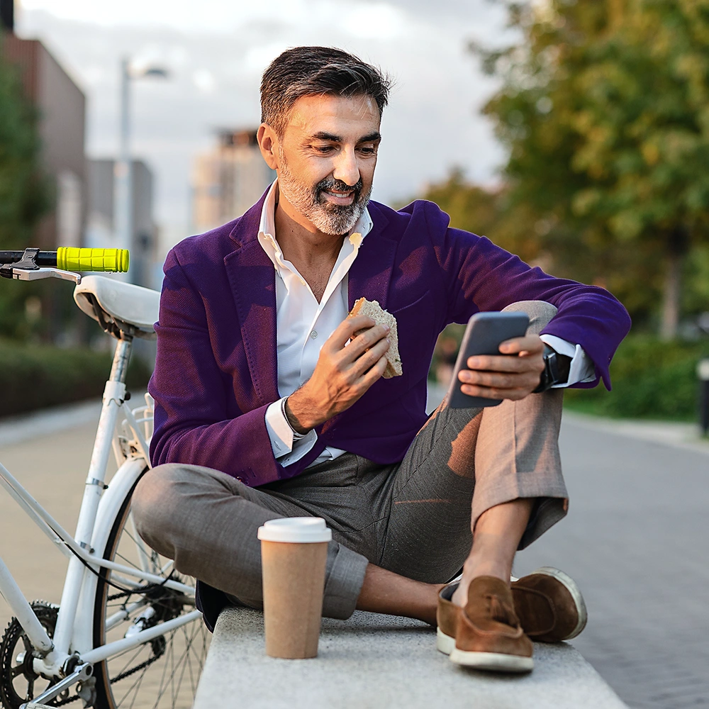 linexo Magazin Mann sitzt mit Smartphone und Kaffee auf einer Bank neben seinem Fahrrad