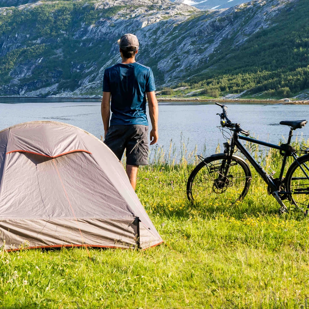 Mann macht Urlaub mit Zelt und Fahrrad am Seeufer in der Natur