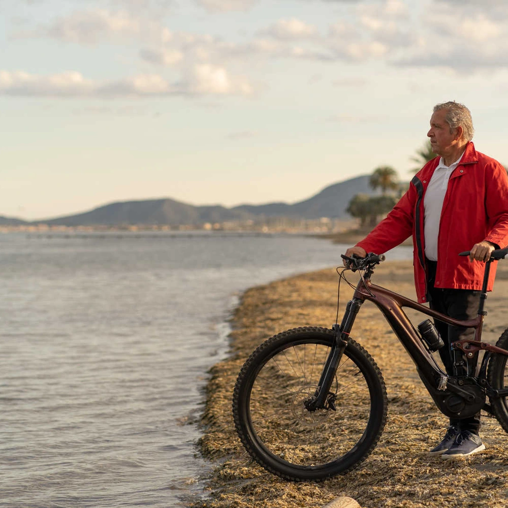 Mann steht mit Mountainnbike am Strand