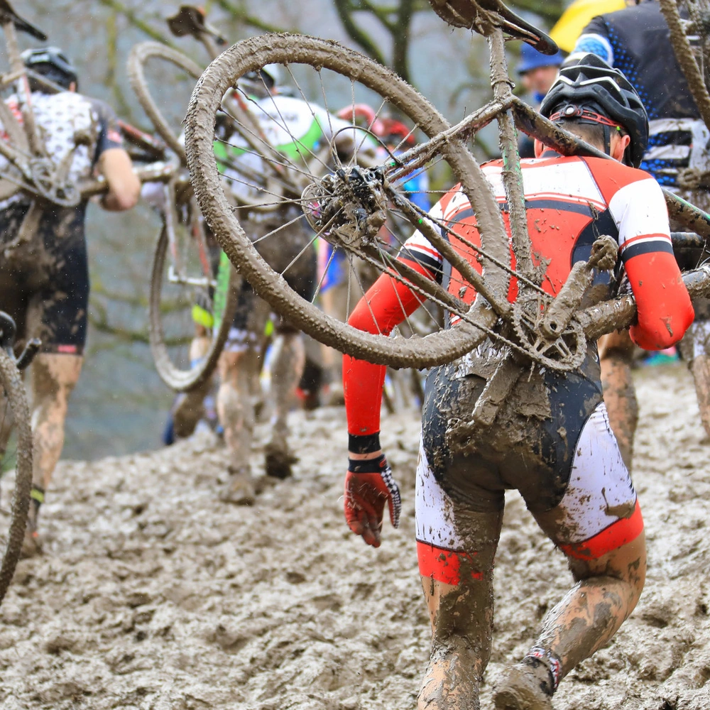 Die Fahrrad-Rennsportdisziplin Cyclocross im Überblick Radsportler laufen durch Schlamm mit ihren Fahrrädern