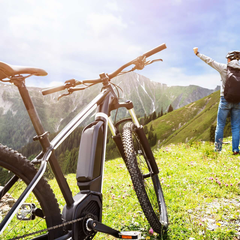 E-Bike-Antrieb: Welche Unterschiede gibt es? Person steht mit dem Rücken zum Betrachter auf einer grünen Wiese und hebt die arme. Das E-Bike steht im Vordergrund.