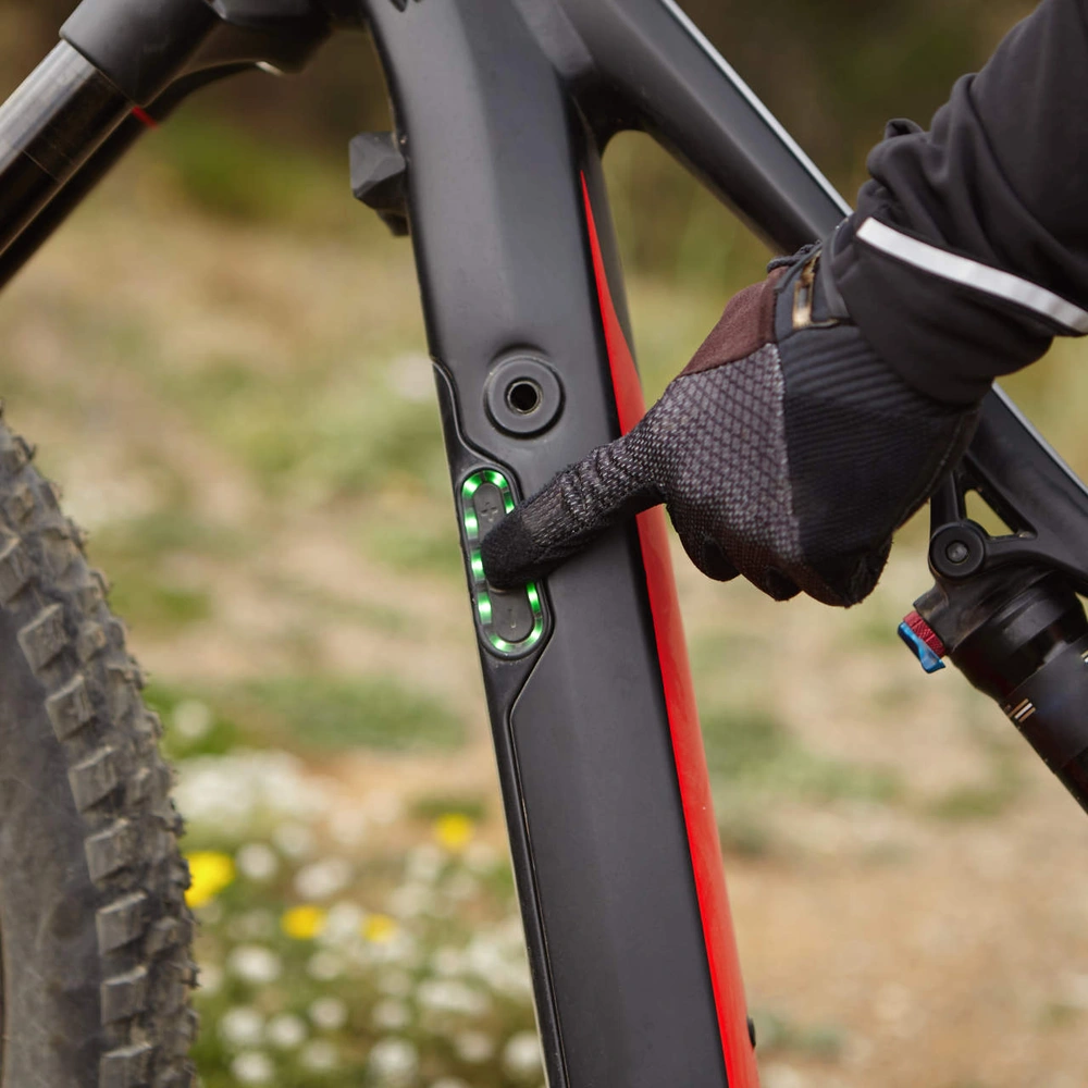 Eine Person in Handschuhen drückt einen Knopf an einem E-Bike-Rahmen