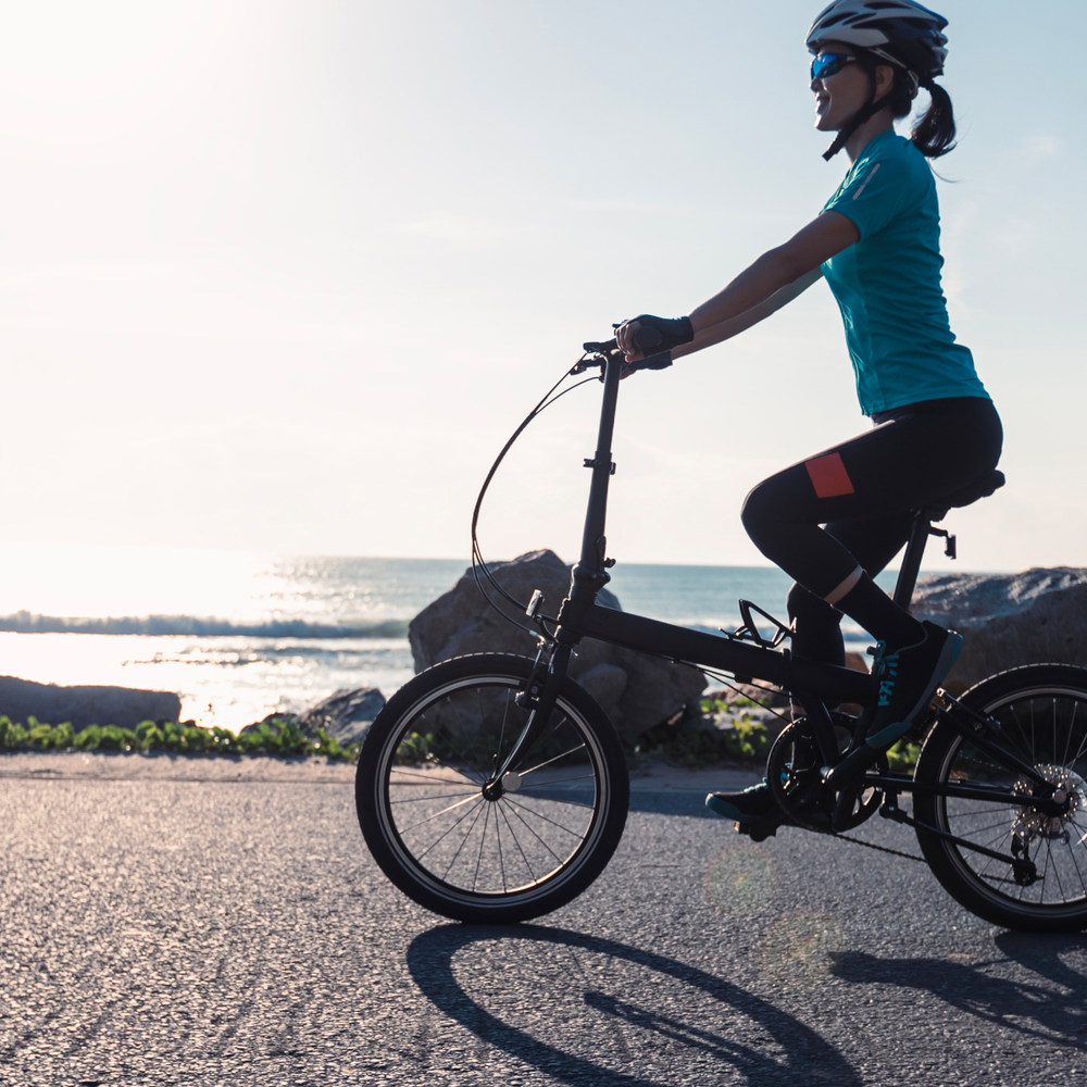 Der große E-Bike Klapprad Test: Die besten Modelle Frau fährt auf einem Klapprad am Meer entlang