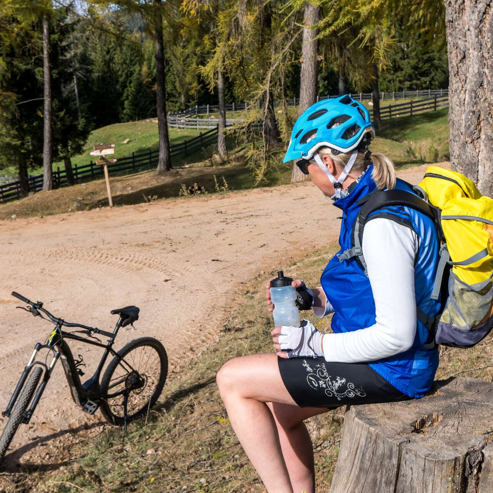 E-Bike Kleidung: Gut geschützt in den Sattel Frau sitzt. Trägt Sportkleidung und einen Fahrradhelm. Im Hintergrund steht ein E-Bike.