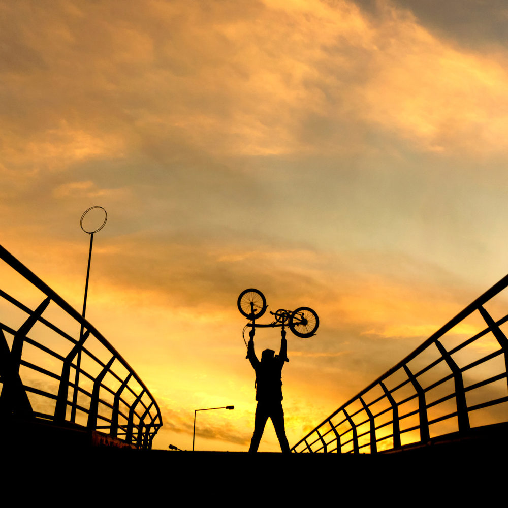 Engwe E-Bike Test – Innovation trifft auf Alltagstauglichkeit Mann auf einer Brücke hält ein Faltrad in die Luft im Sonnenuntergang