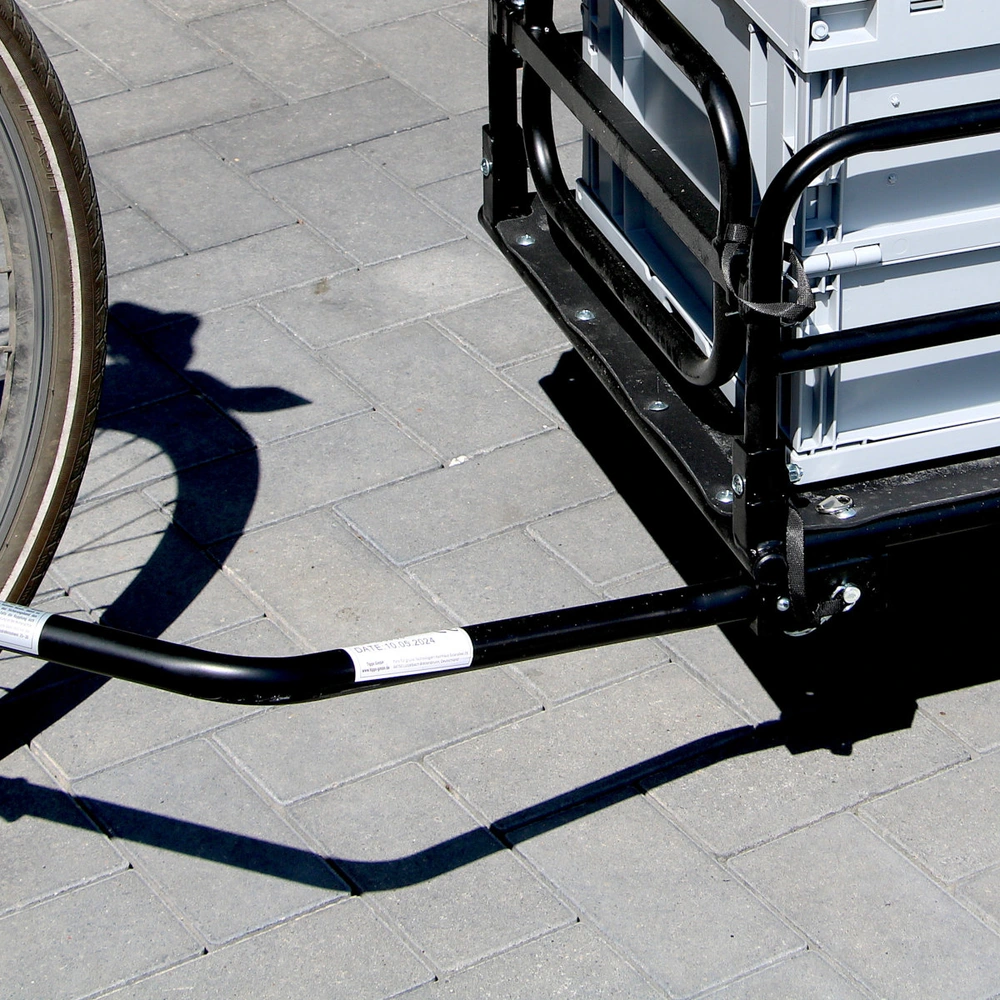 Fahrradanhänger mit Verbindung zu einem Fahrrad auf Pflastersteinen.