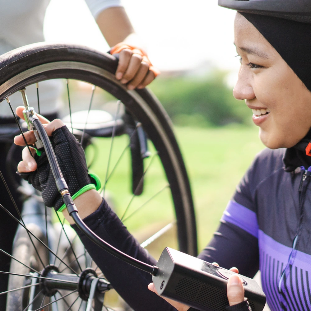 Fahrradpumpen Test 2025 Frau kniet neben einem Fahrrad und Pumpt mit einer Fahrradpumpe den Reifen auf