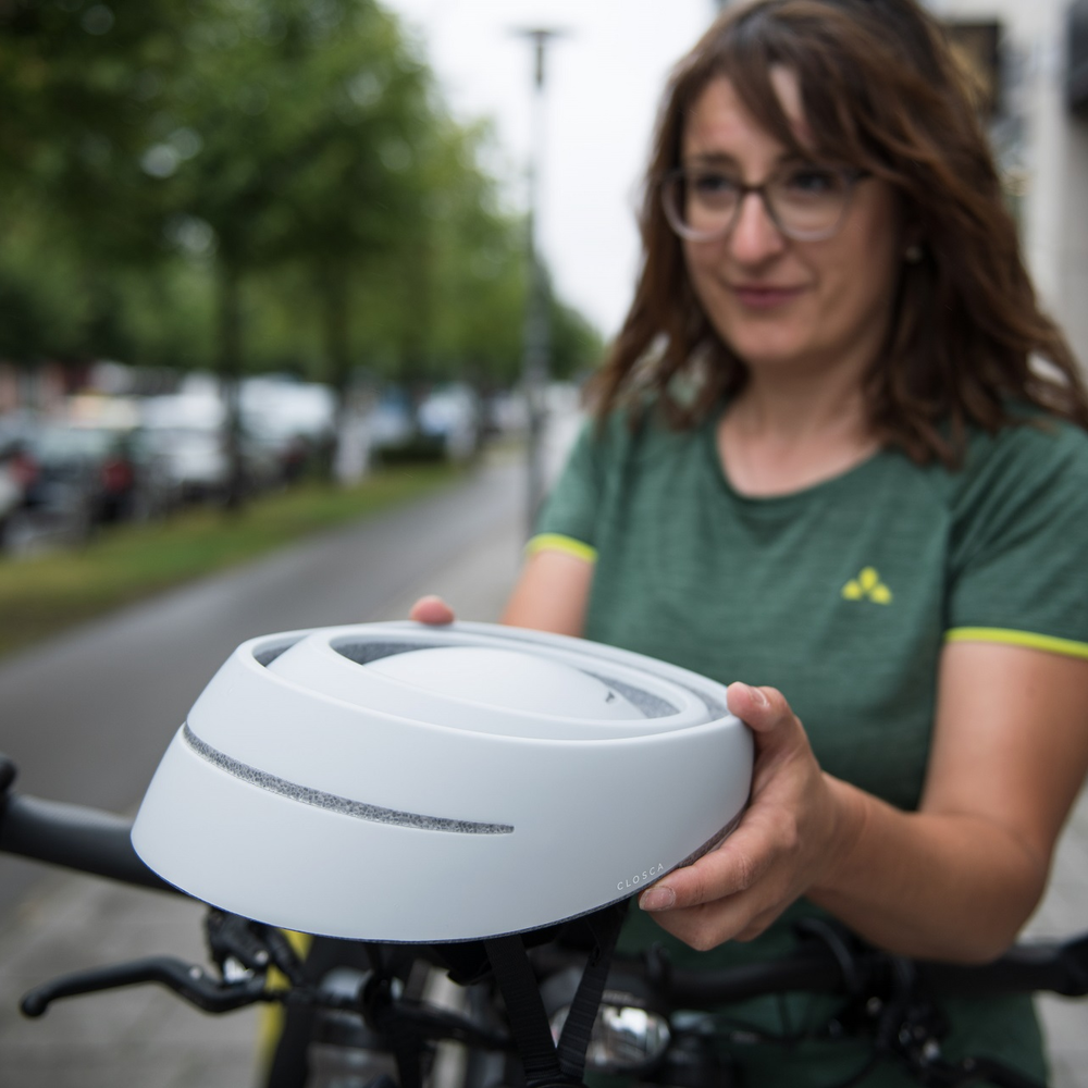 Falthelm des spanischen Herstellers Closca Radfahrerin hält zusammengefalteten Helm von Closca in der Hand.