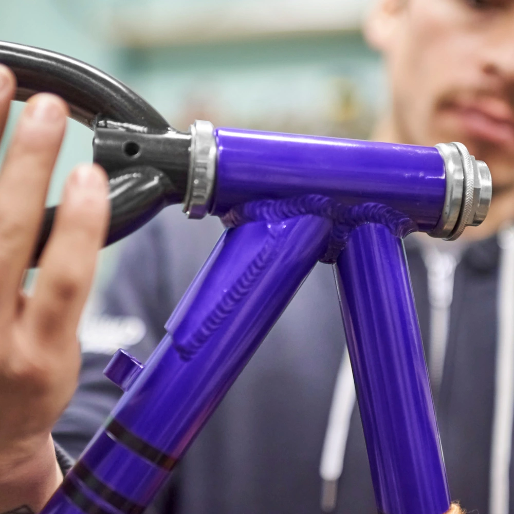 Hände montieren Teile an einem lila Fahrradrahmen in einer Werkstatt.