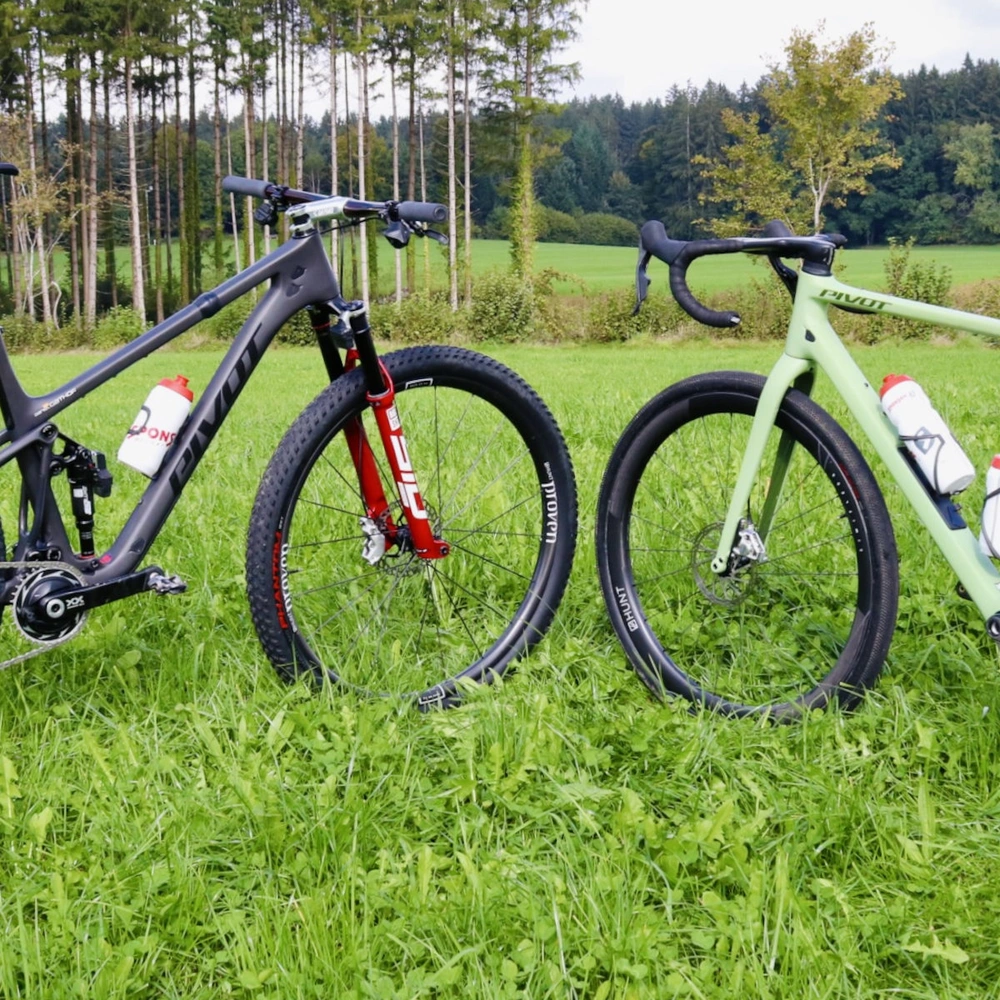 Zwei Fahrräder stehen auf grünem Gras vor einem Wald, ein schwarzes und ein grünes.
