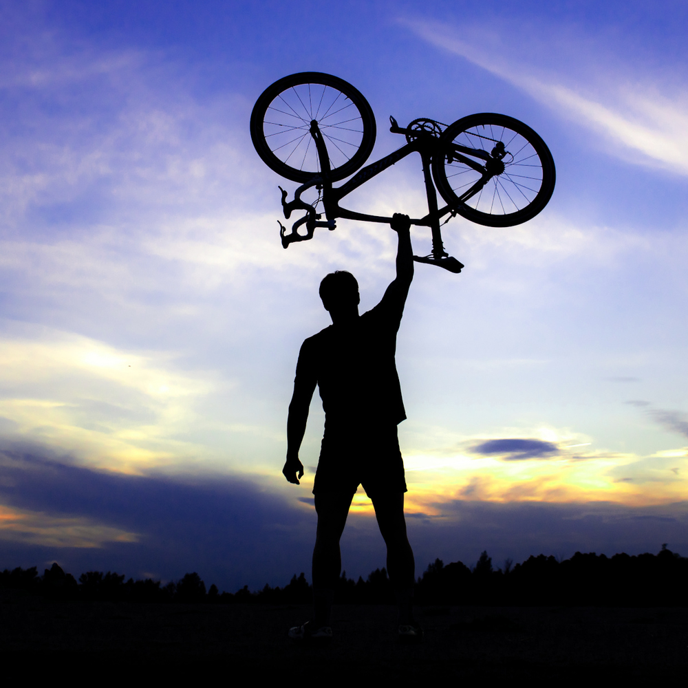 Hardtail oder Fully: Der Vergleich Mann hält ein Mountainbike in den Himmel