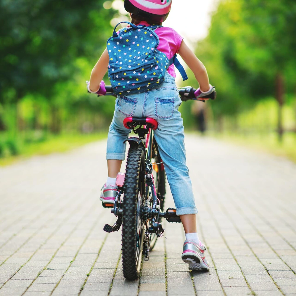 Mädchen mit Rucksack und Helm fährt auf einem Kinderfahrrad einen gepflasterten Weg entlang