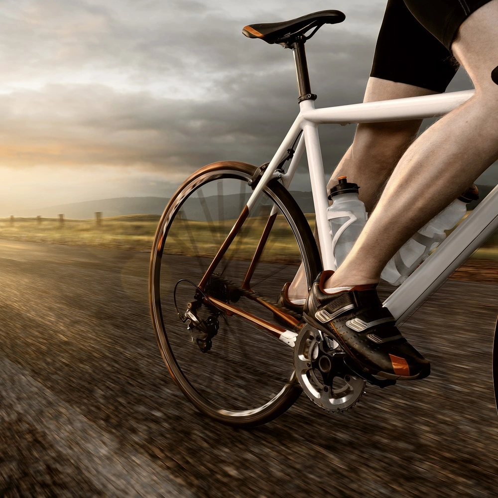 Bei Klickpedalen sind Schuh und Pedale fest miteinander verbunden. Weißes Rennrad auf einer Straße, von dessen Fahrer Beine und Schuhe auf den Pedalen sichtbar sind.