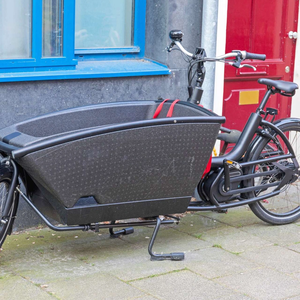 Dunkles Lastenrad mit abgerundetem Kasten steht an einer Hauswand