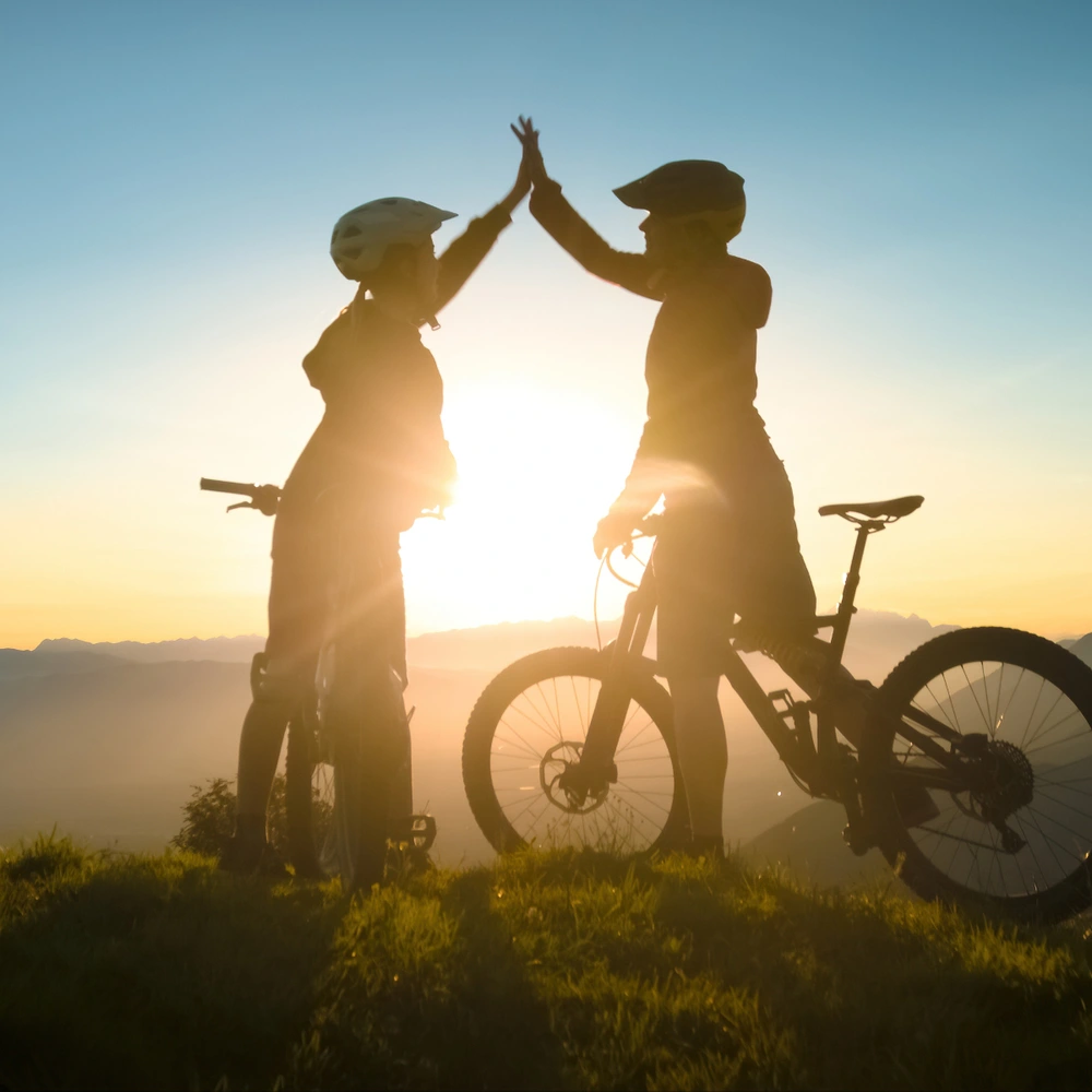 Zwei Frauen schlagen ein im Sonnenuntergang auf dem Fahrrad in den Bergen