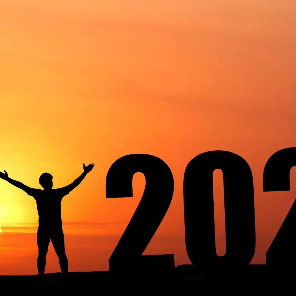 Silhouette einer Person mit Fahrrad vor der untergehenden Sonne und der Zahl 2026.