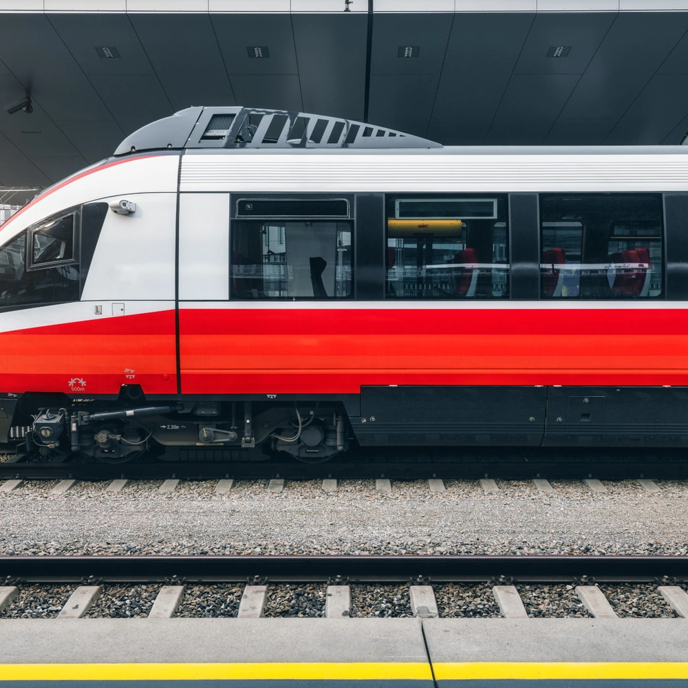 Ein moderner Zug in Rot und Weiß steht am Bahnsteig.